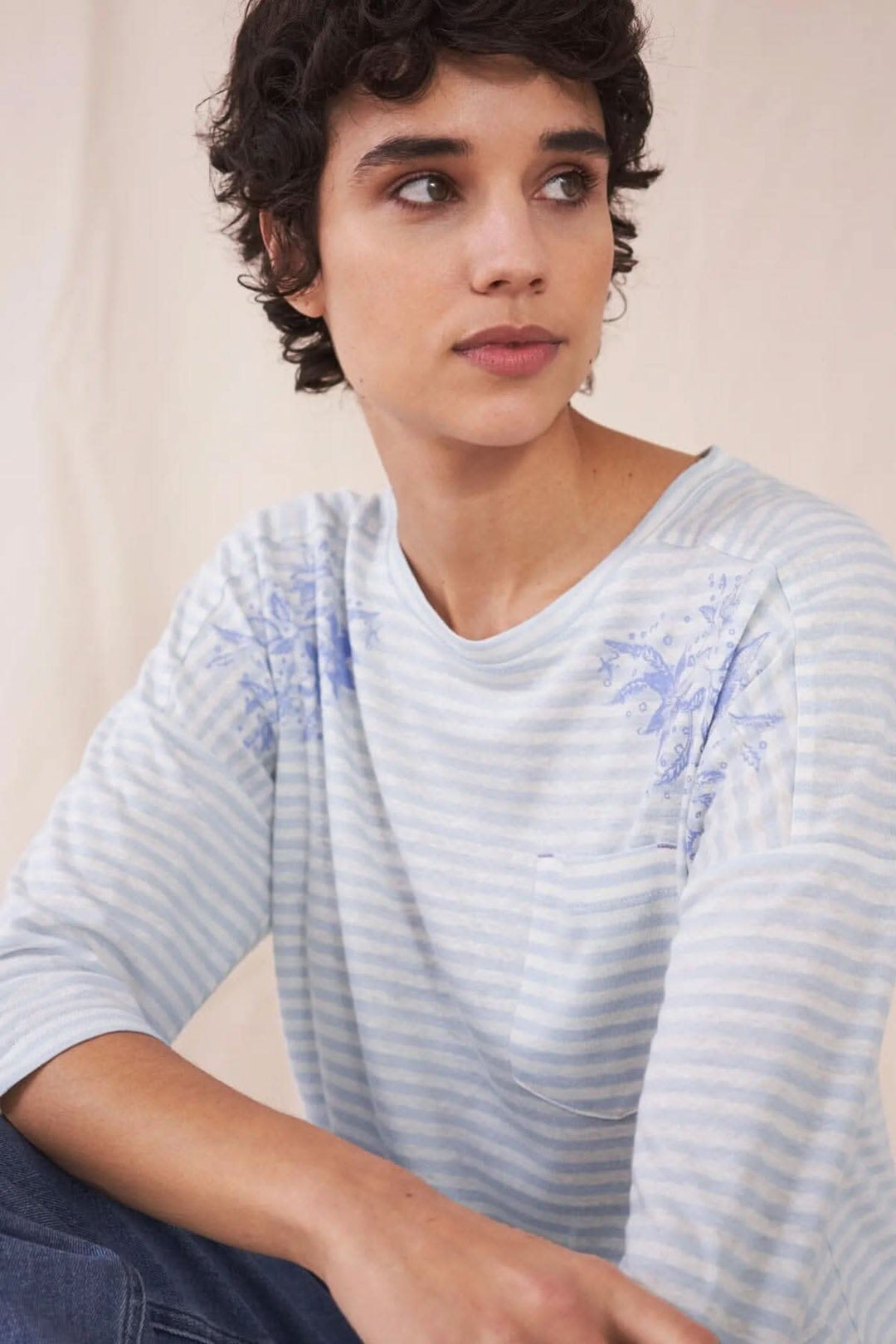 Femme portant un t-shirt léger rayé bleu avec motifs floraux, parfait pour un style décontracté et frais.